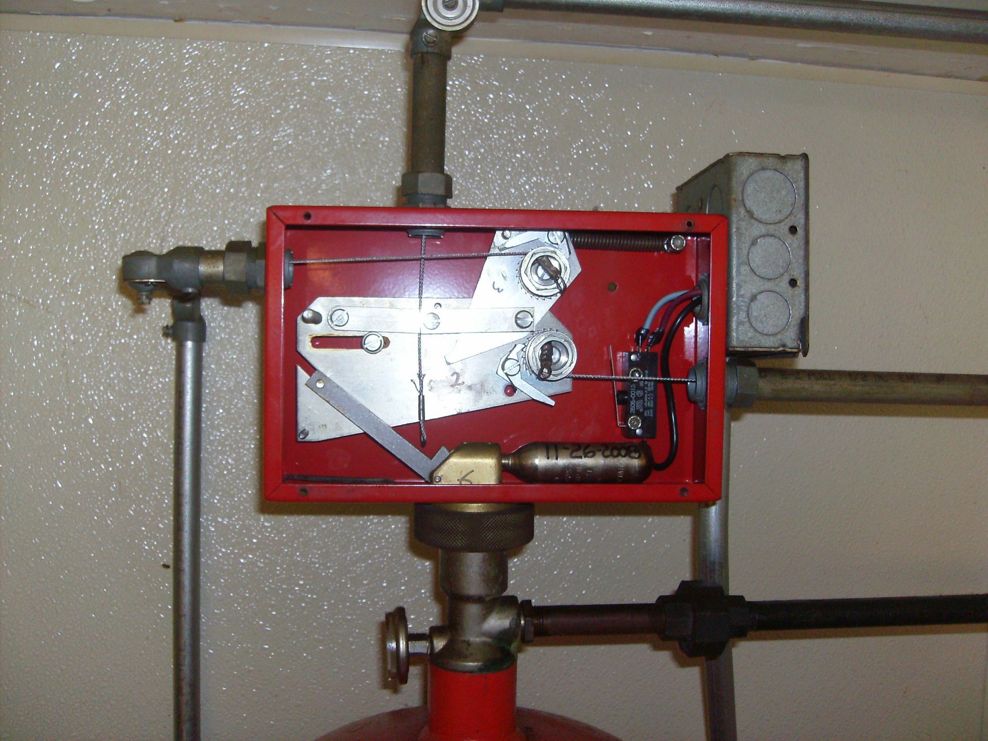 Red fire suppression system control box mounted on pipes.