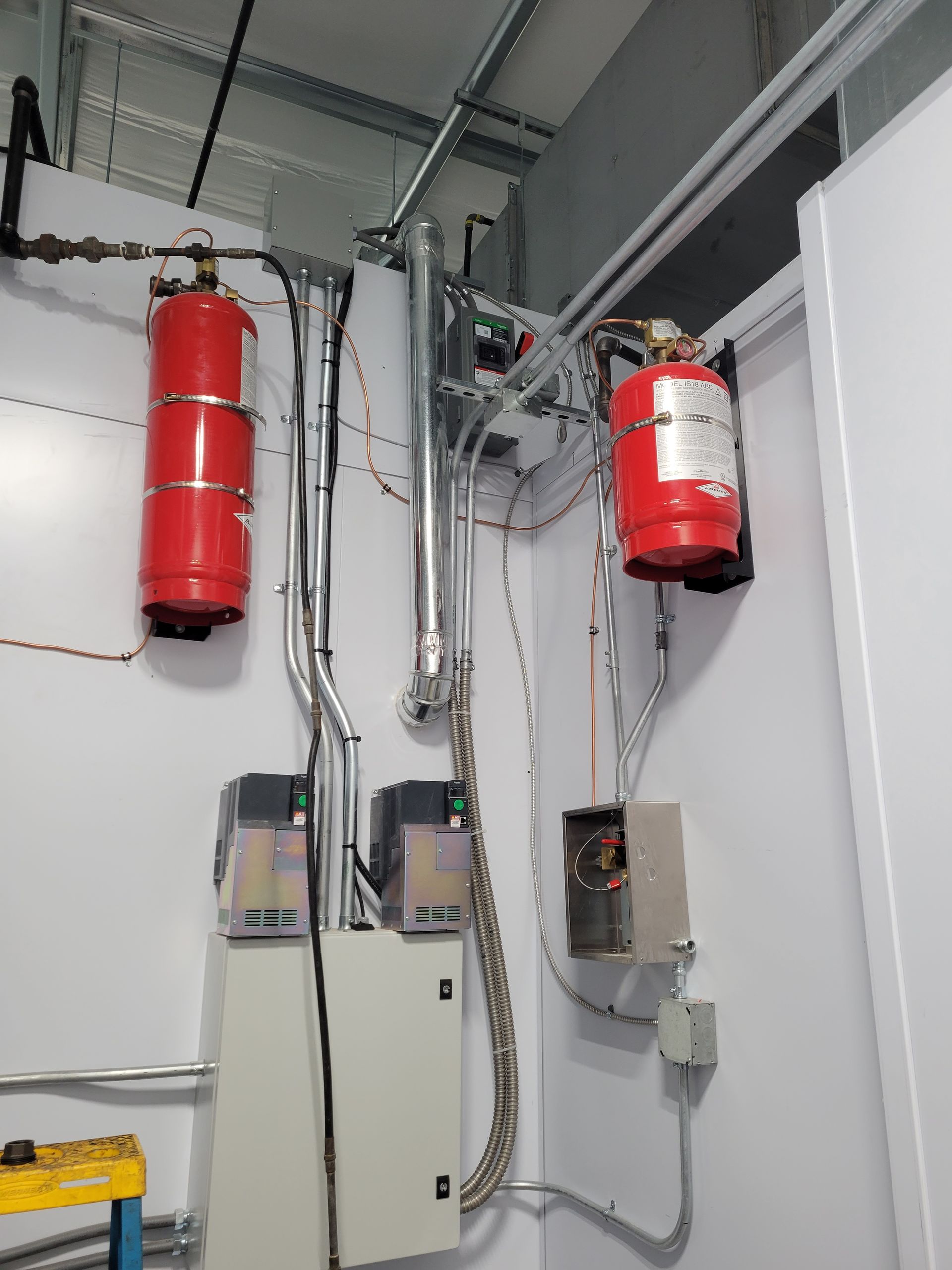 Red fire suppression tanks and electrical equipment mounted on a white wall in a building.