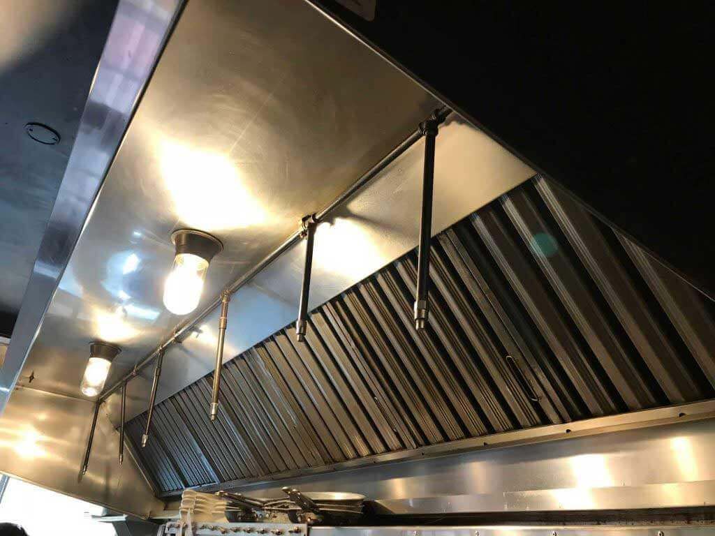 Stainless steel commercial kitchen exhaust hood with lights and metal filters.