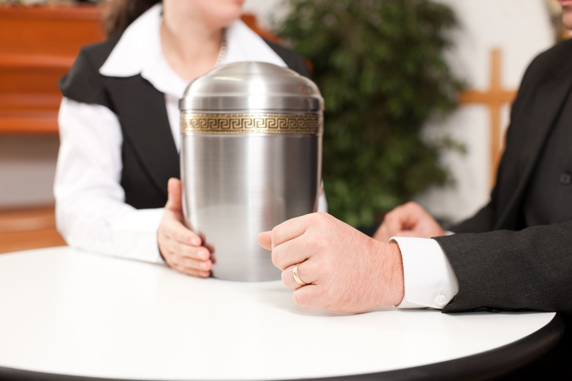 A partial view of a man and a woman engaged in conversation with a silver urn placed between them.
