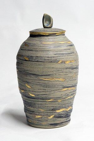 A gray and gold vase with a lid on a white background.