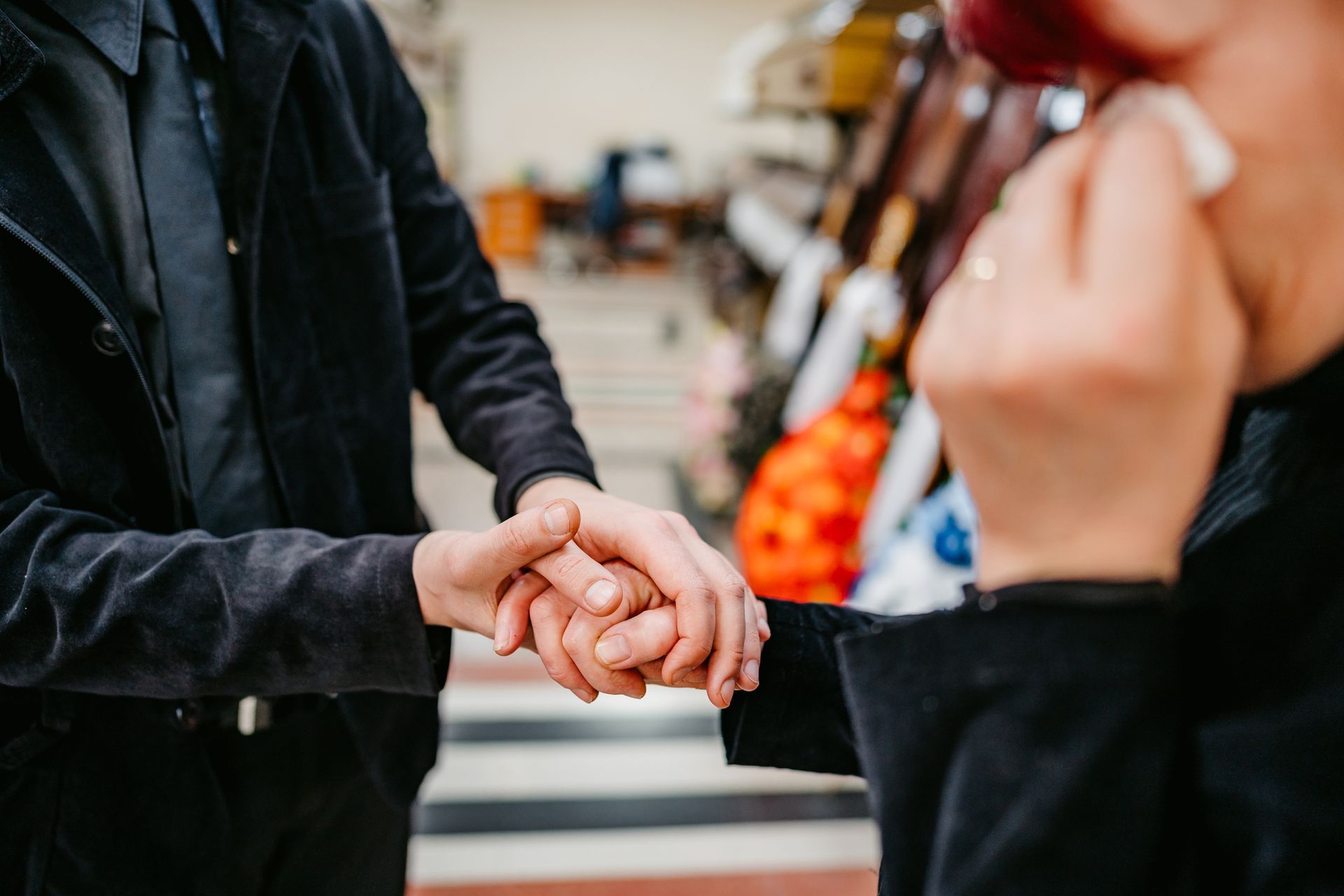 Person holding another's hand in a funeral home with coffins in the background.