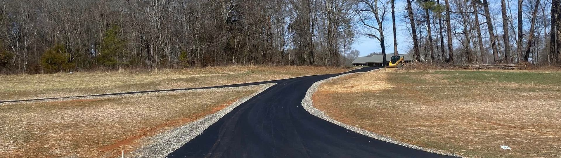 Winding black paved path through dry grass and leafless trees on a sunny day