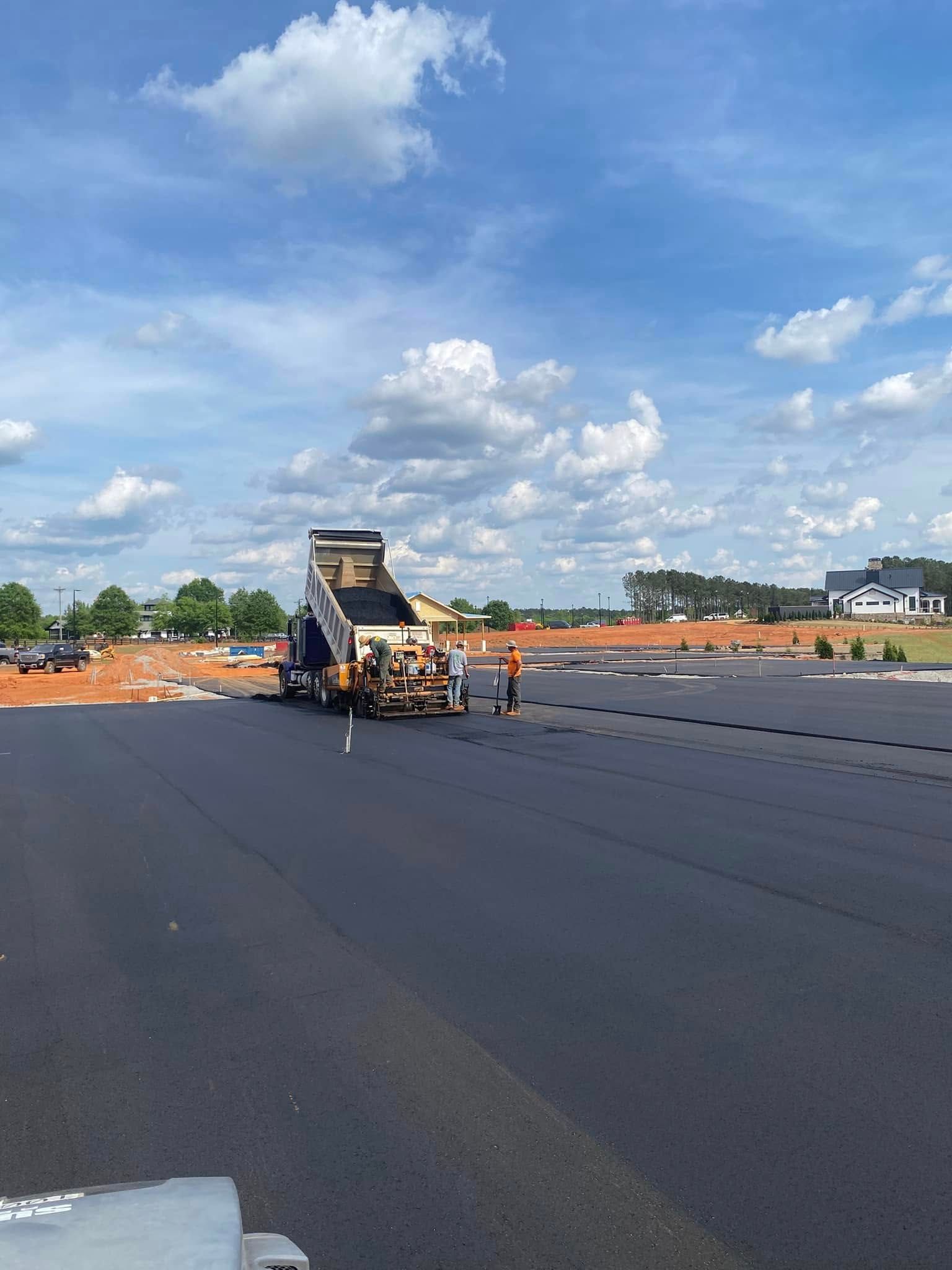 Road paving machine laying fresh black asphalt on a wide roadway under a blue sky