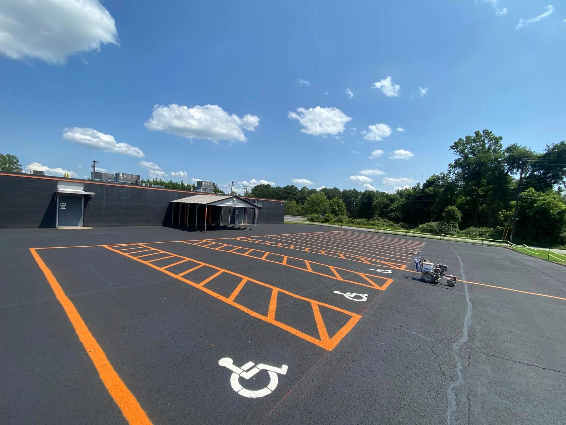 Outdoor parking lot with orange marked accessible spaces under a blue sky, near a building and trees