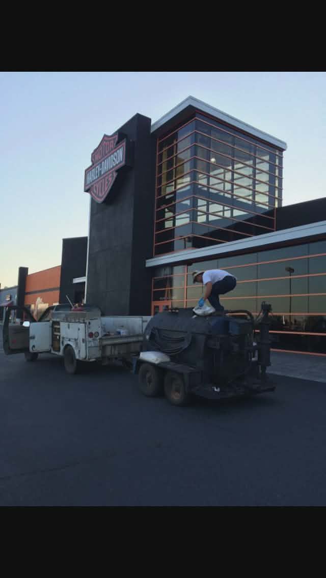 A pickup towing two trailers passes a glass-fronted building at dusk.