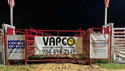 Red rodeo gate with sponsor banners, including VAPCO and Coors, at night
