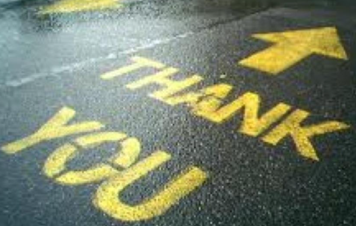 Yellow “THANK YOU” and arrow painted on wet pavement at night.