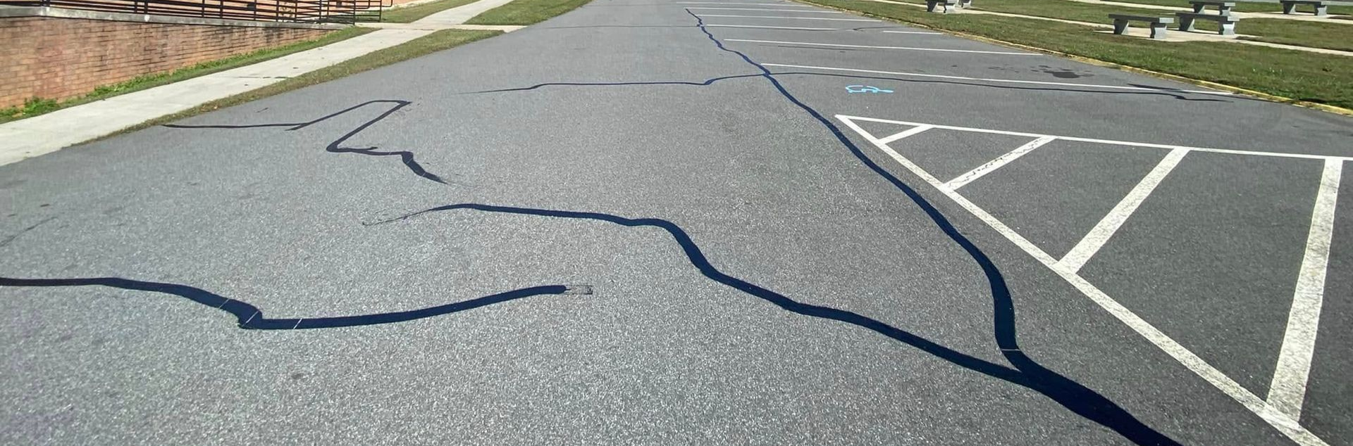 Cracked asphalt road with lane markings and parking spaces along the right side