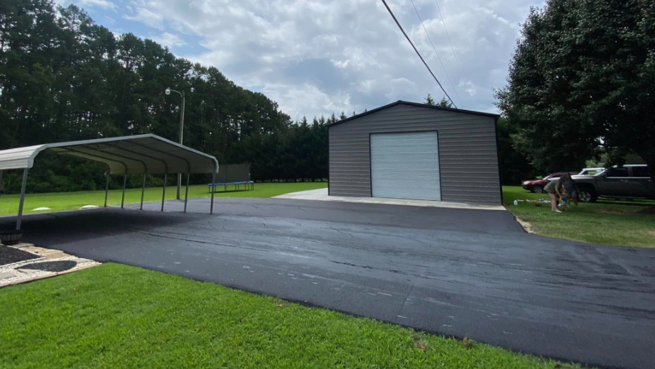 Parking lot with a gray metal shed, covered canopy, and trees under a cloudy sky
