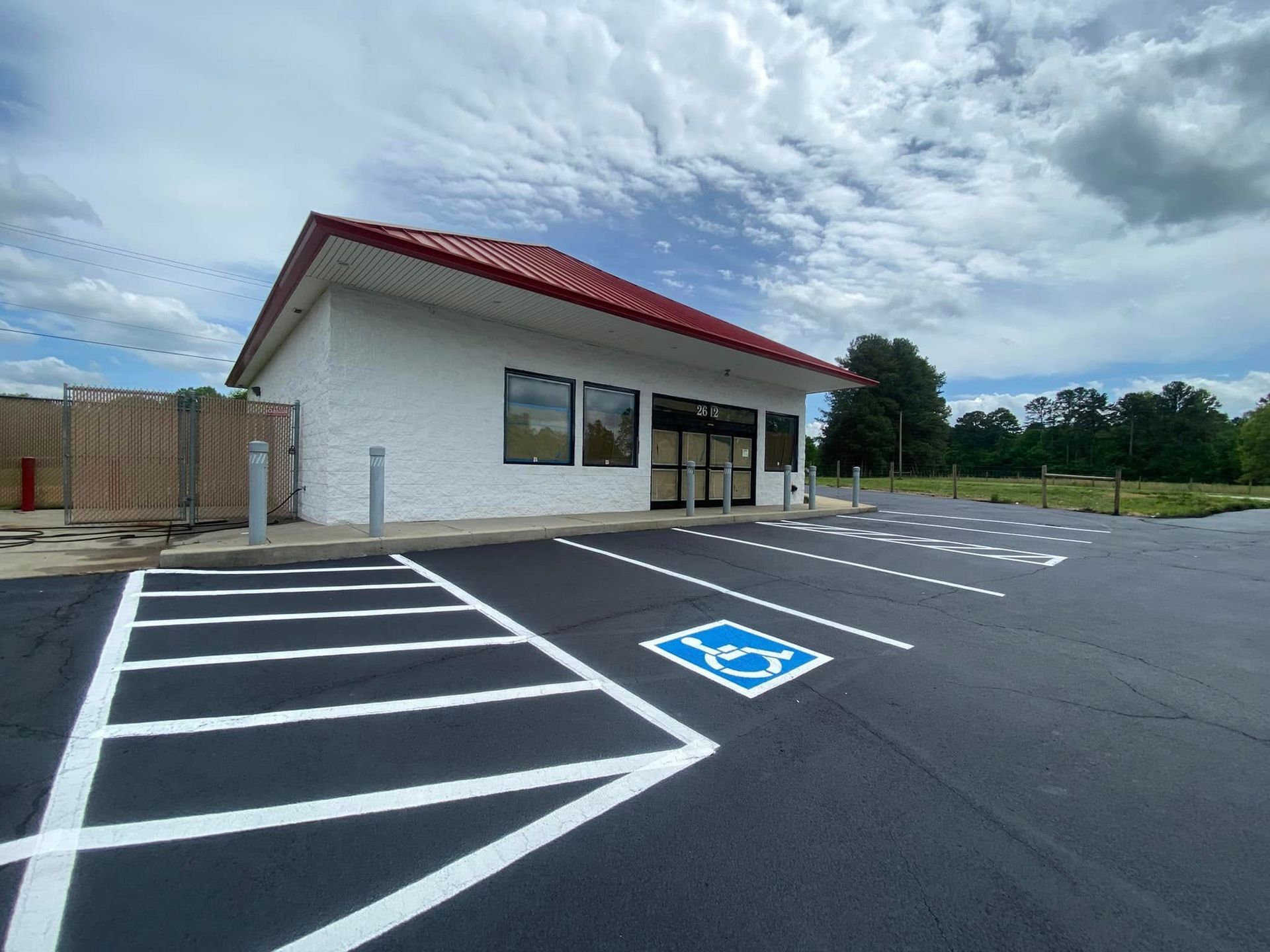 Empty parking lot beside a small white building with a red roof and accessible parking space marked in blue.