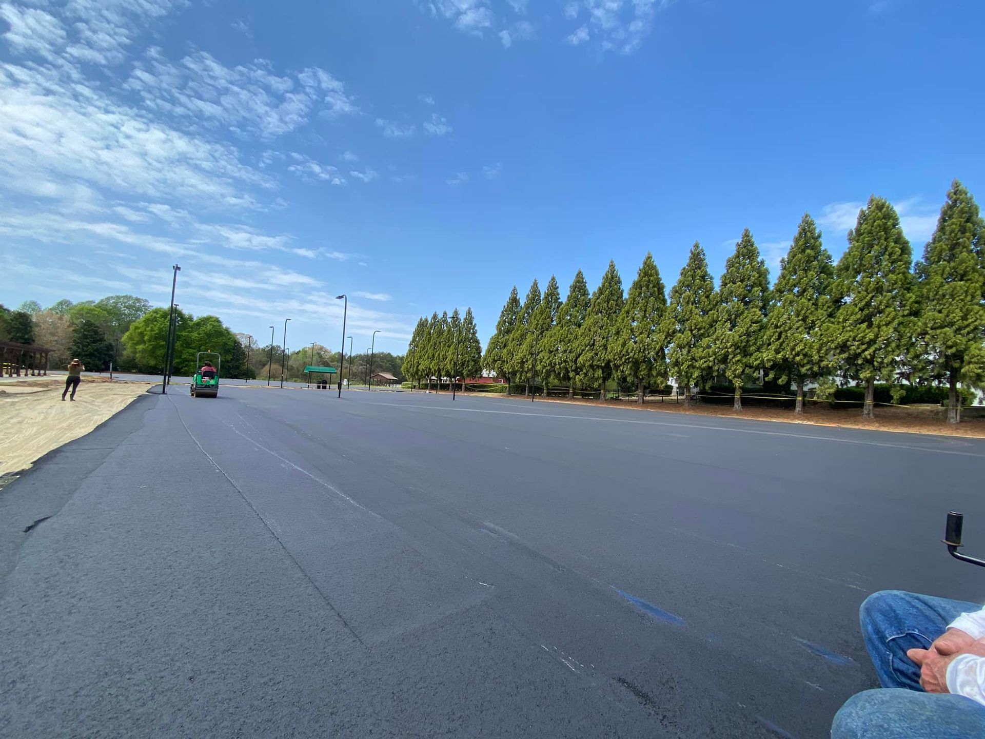 Wide open paved plaza beside rows of trees under a blue sky, with a few people in the distance