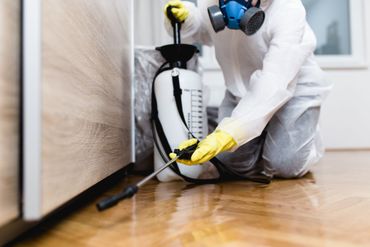 An exterminator in a protective, white uniform and yellow gloves, performing pest control service.
