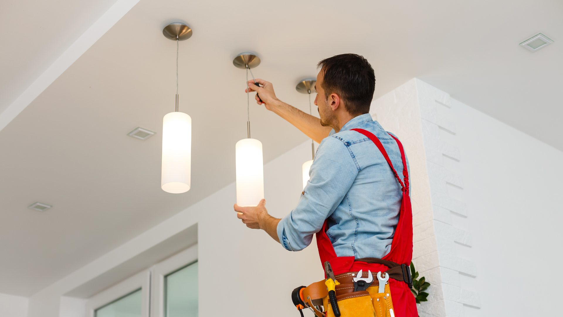 A man is installing a light fixture on the ceiling.