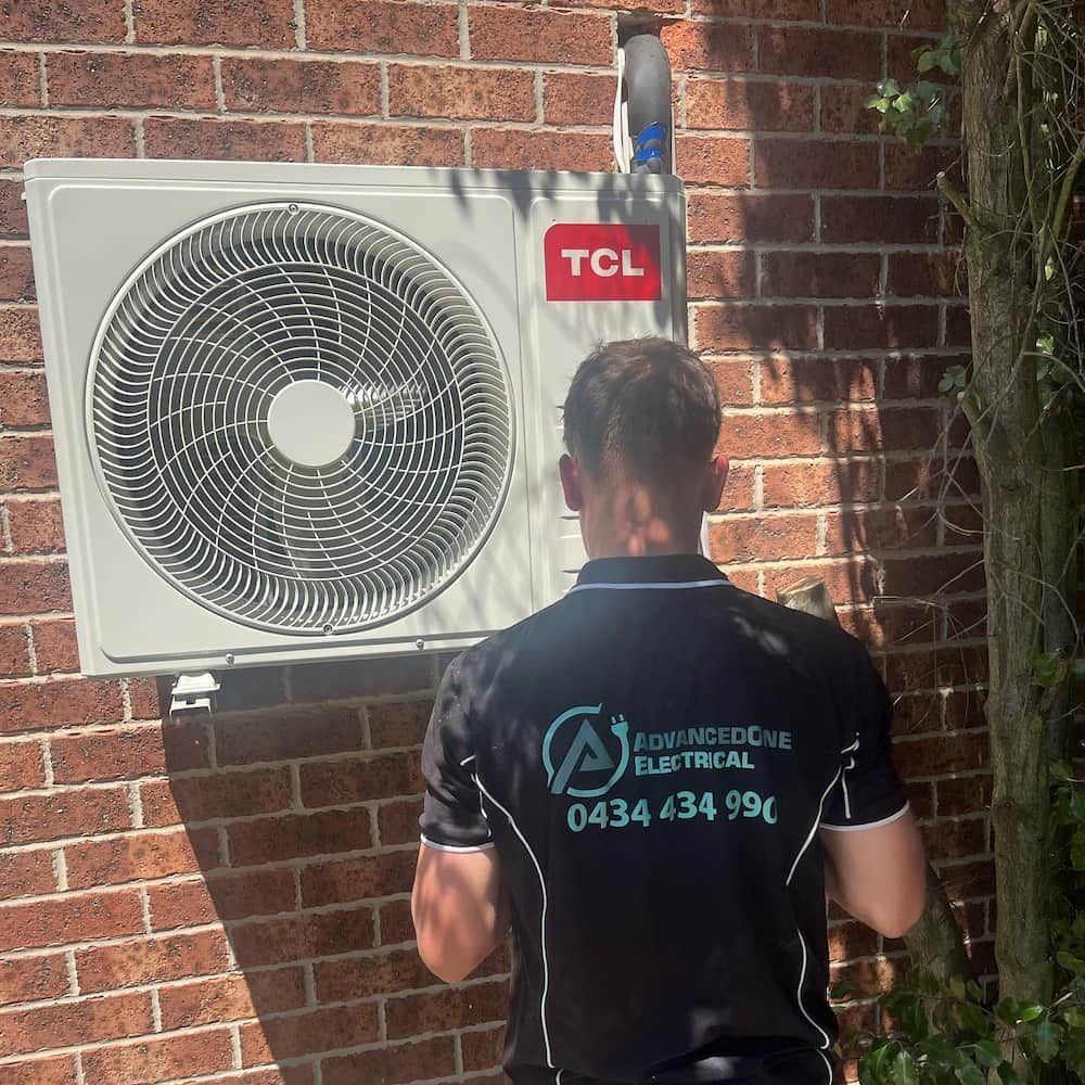 A Man Standing Next To A TCL Fan On A Brick Wall — AdvancedOne Electrical in Alfredton, VIC