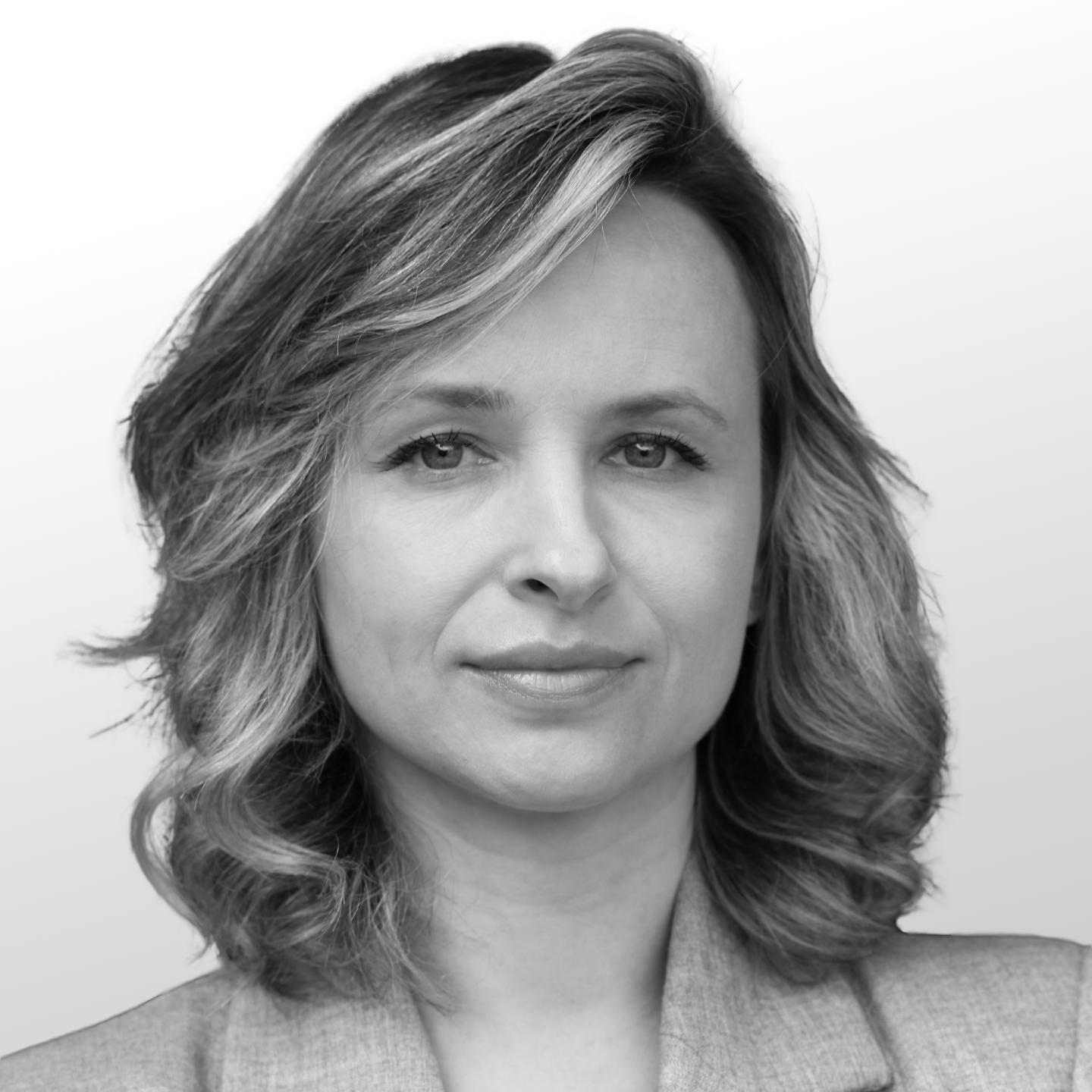 Smiling woman in a black blazer and pearl necklace against a dark background.