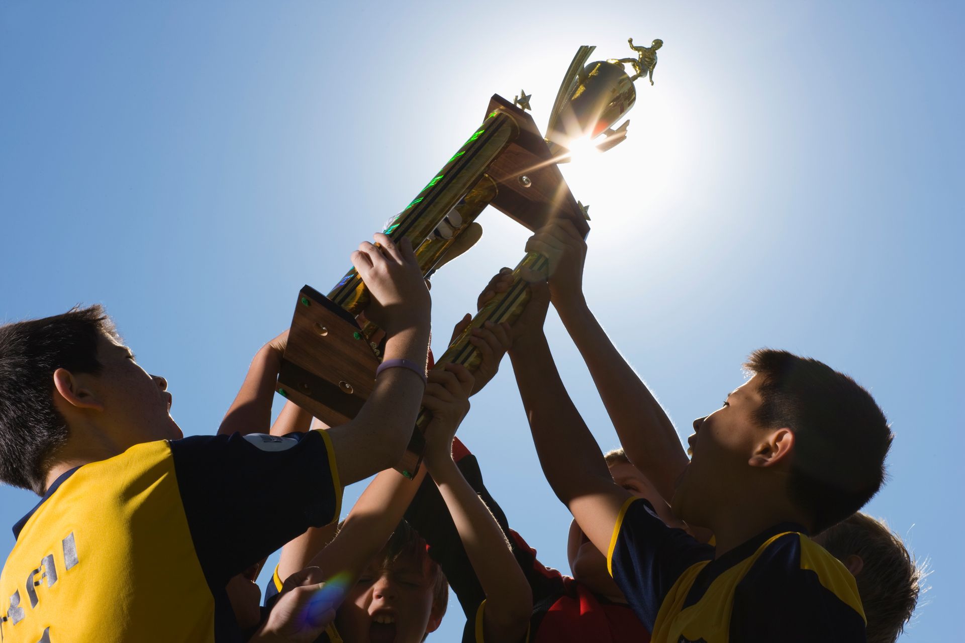 People lifting a trophy overhead outdoors against a bright blue sky