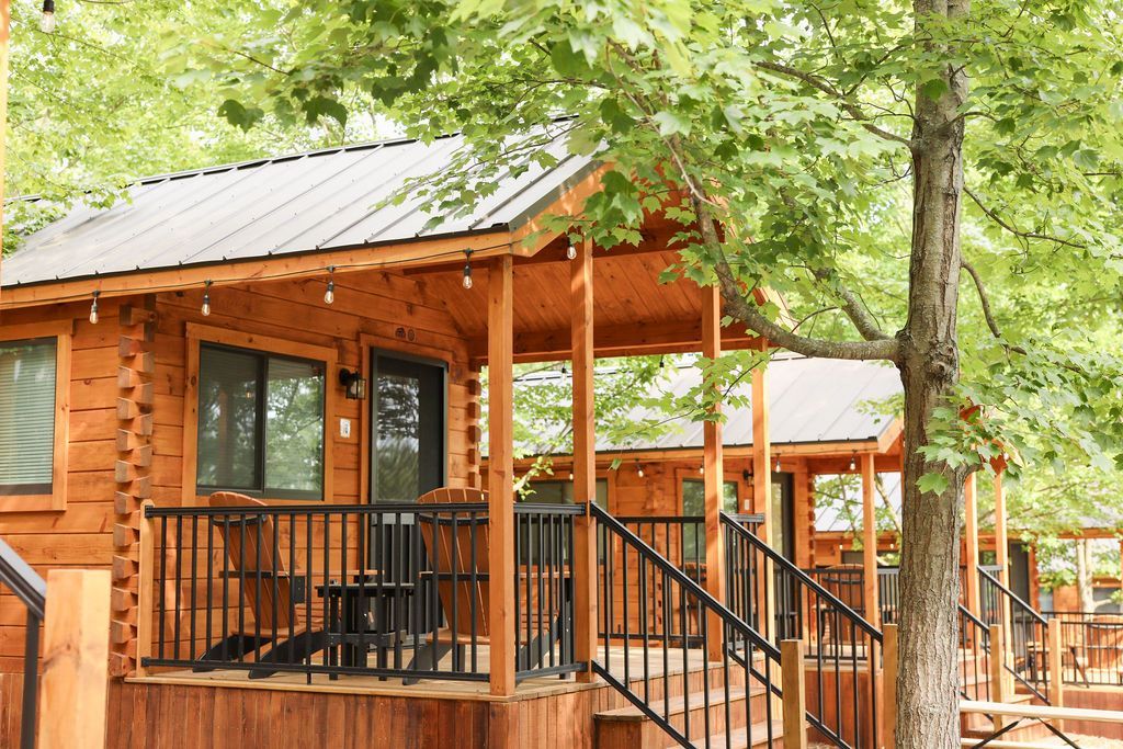 A log cabin with a porch and stairs is surrounded by trees.