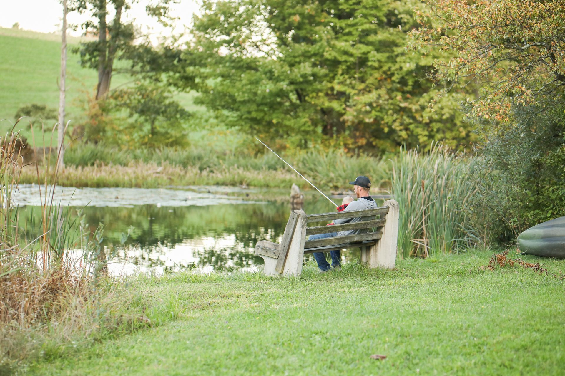 A man is sitting on a bench fishing in a pond.