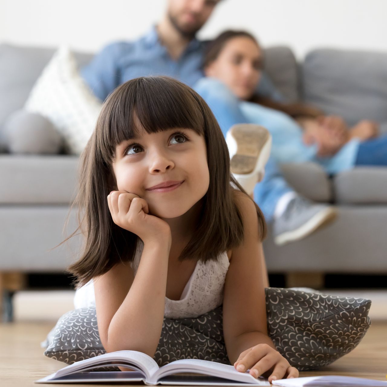 A little girl is laying on the floor reading a book