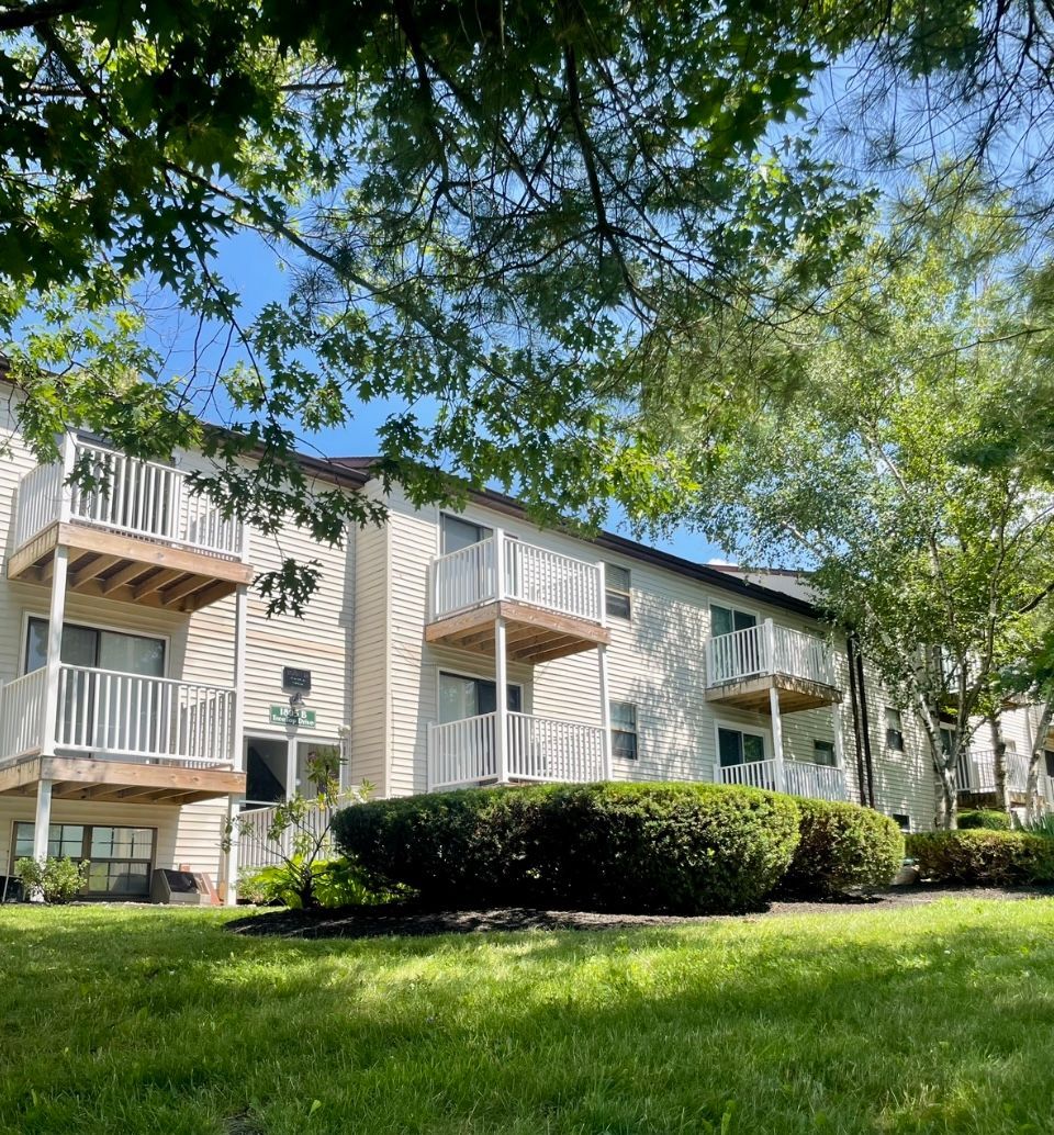 A white apartment building with balconies and trees in front of it.