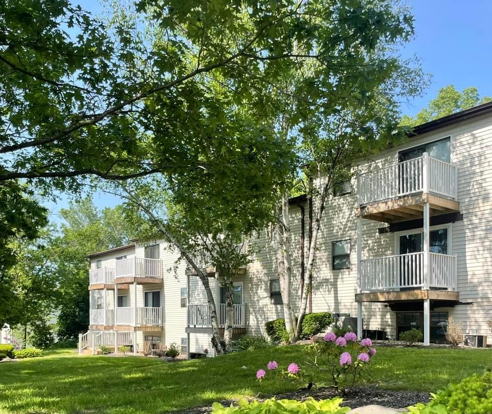 A white apartment building with balconies and trees in front of it.