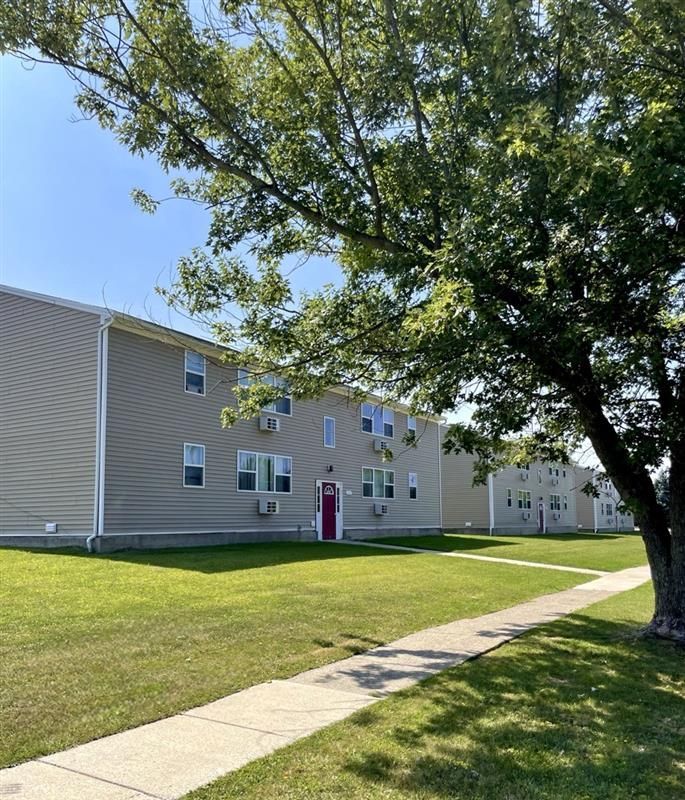 A large apartment building with a sidewalk and a tree in front of it.