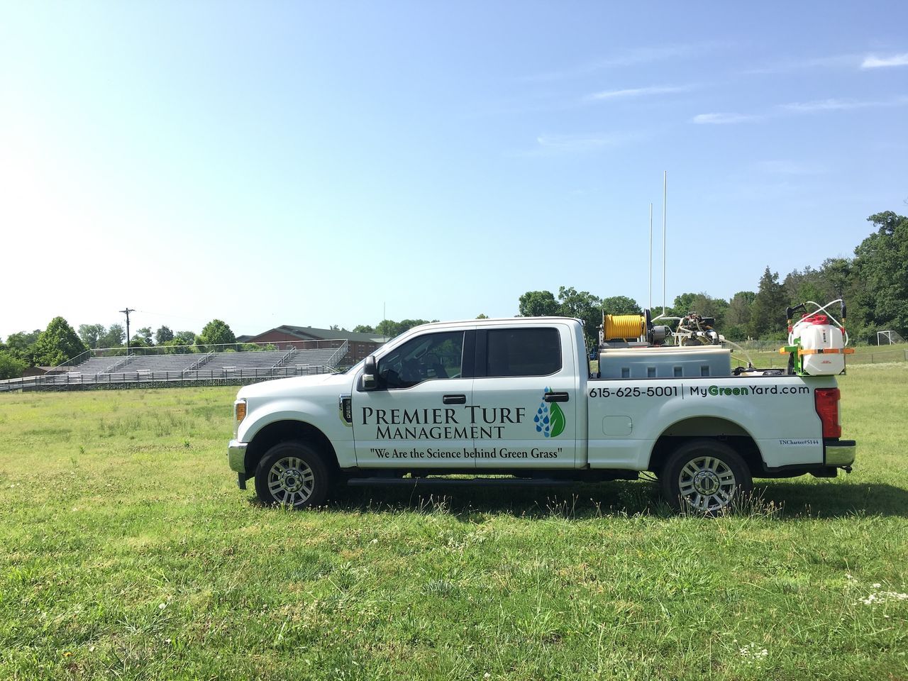 White utility pickup truck with company logos parked on grass beside a road under a clear blue sky