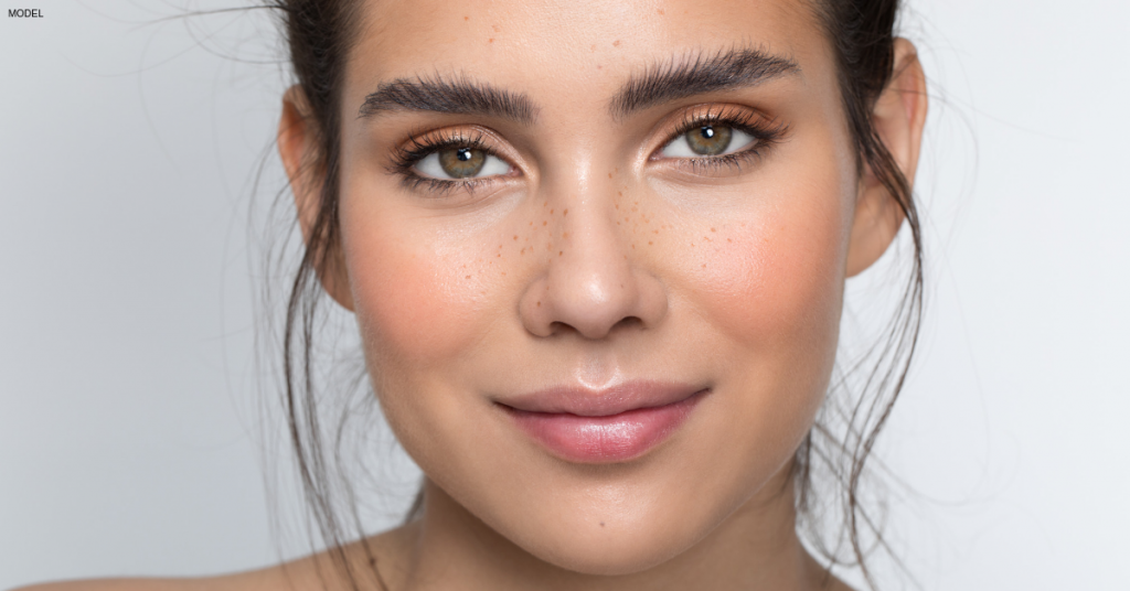 Woman with highlighted skin, light brown eye makeup, and full eyebrows.