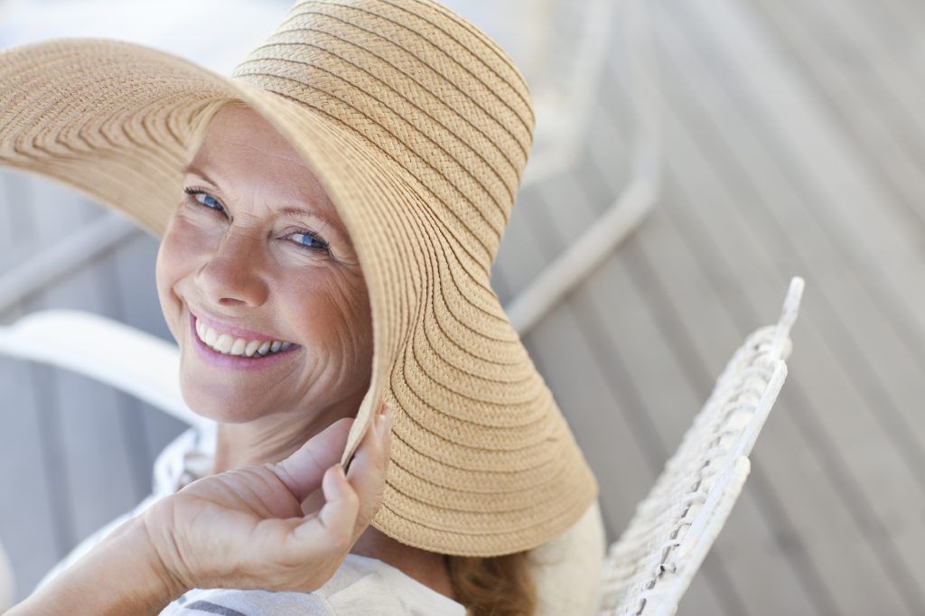 Woman in straw hat smiles, relaxing outdoors, light colors.