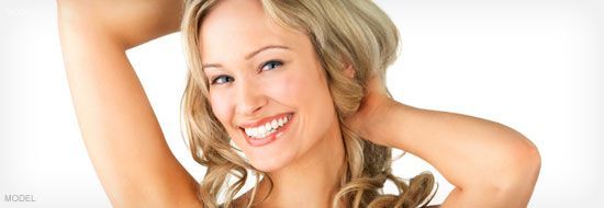 Woman smiling with arms raised behind head, against a white background.