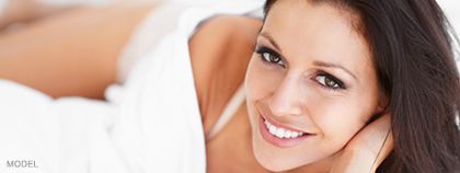 Woman smiling in bed, wrapped in white sheets.