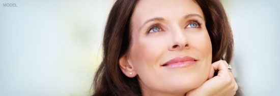 Woman looking up with a thoughtful expression. She is touching her chin, in a soft focus setting.