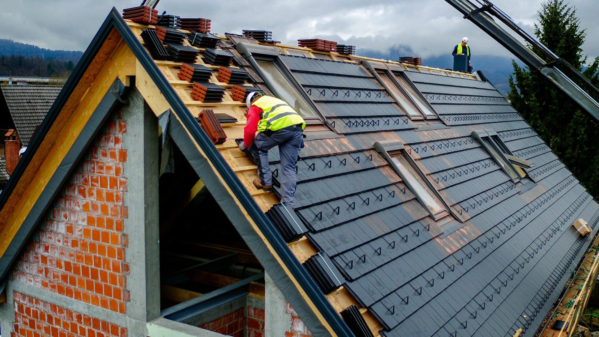 Workers repairing a sloped gray shingle roof with tools and materials stacked along the ridge