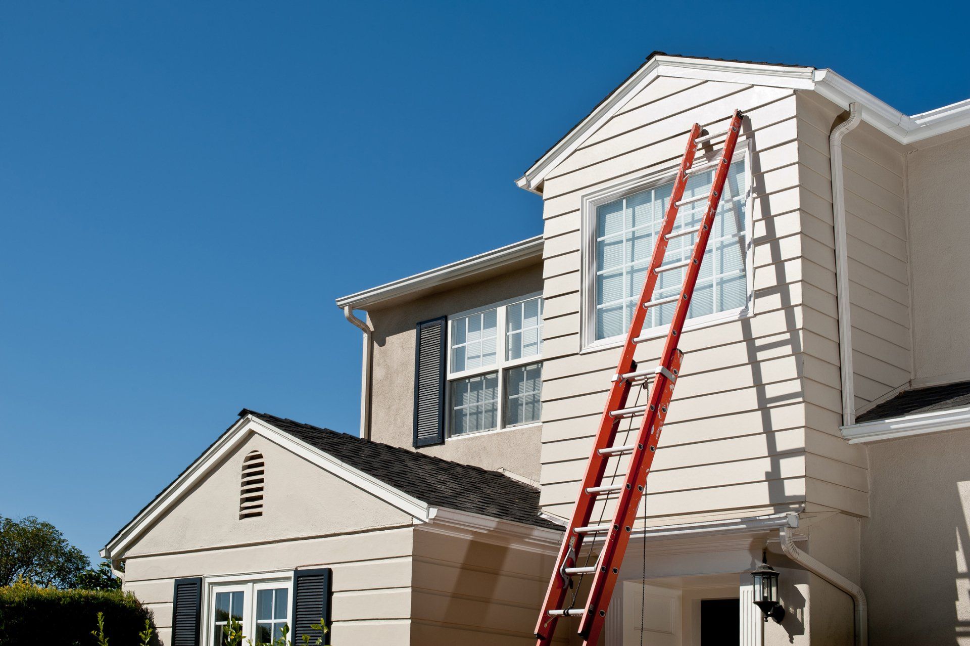 Worker repairing a sloped roof with gray shingles beside a brick house under cloudy skies