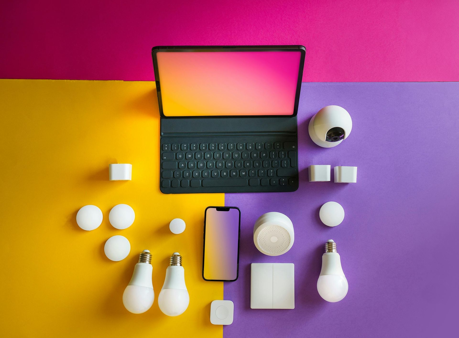 Smart home devices including smart bulbs, security cameras, tablet, and smartphone arranged on a vibrant yellow, pink, and purple background, showcasing modern smart home technology