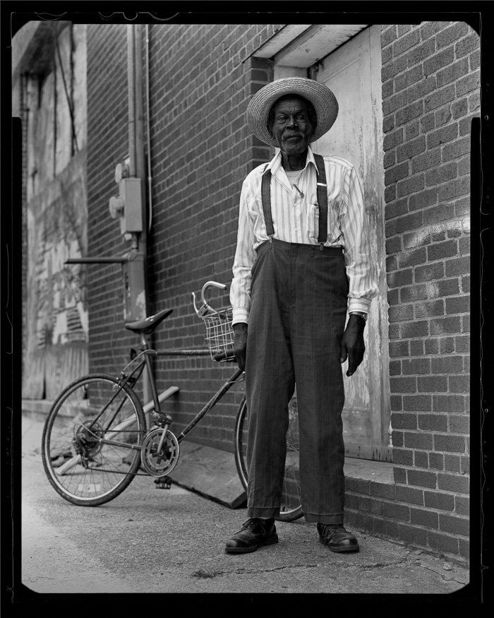 a black and white photo of a man standing next to a bicycle