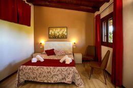 Accogliente camera da letto con copriletto rosso, lampade dai colori caldi, pavimento in legno e ampia finestra con tende rosse.