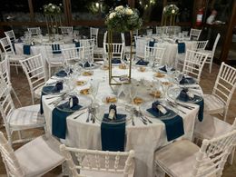 Sala da banchetto decorata con sedie rivestite di bianco, tovaglie rosse e un tetto di legno.