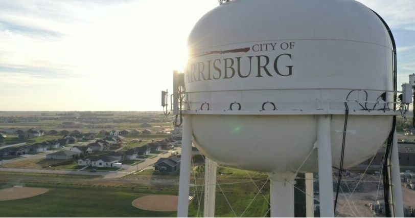 Water tower in Harrisburg, South Dakota, with the city name on it. Sunny day, residential area in the background.