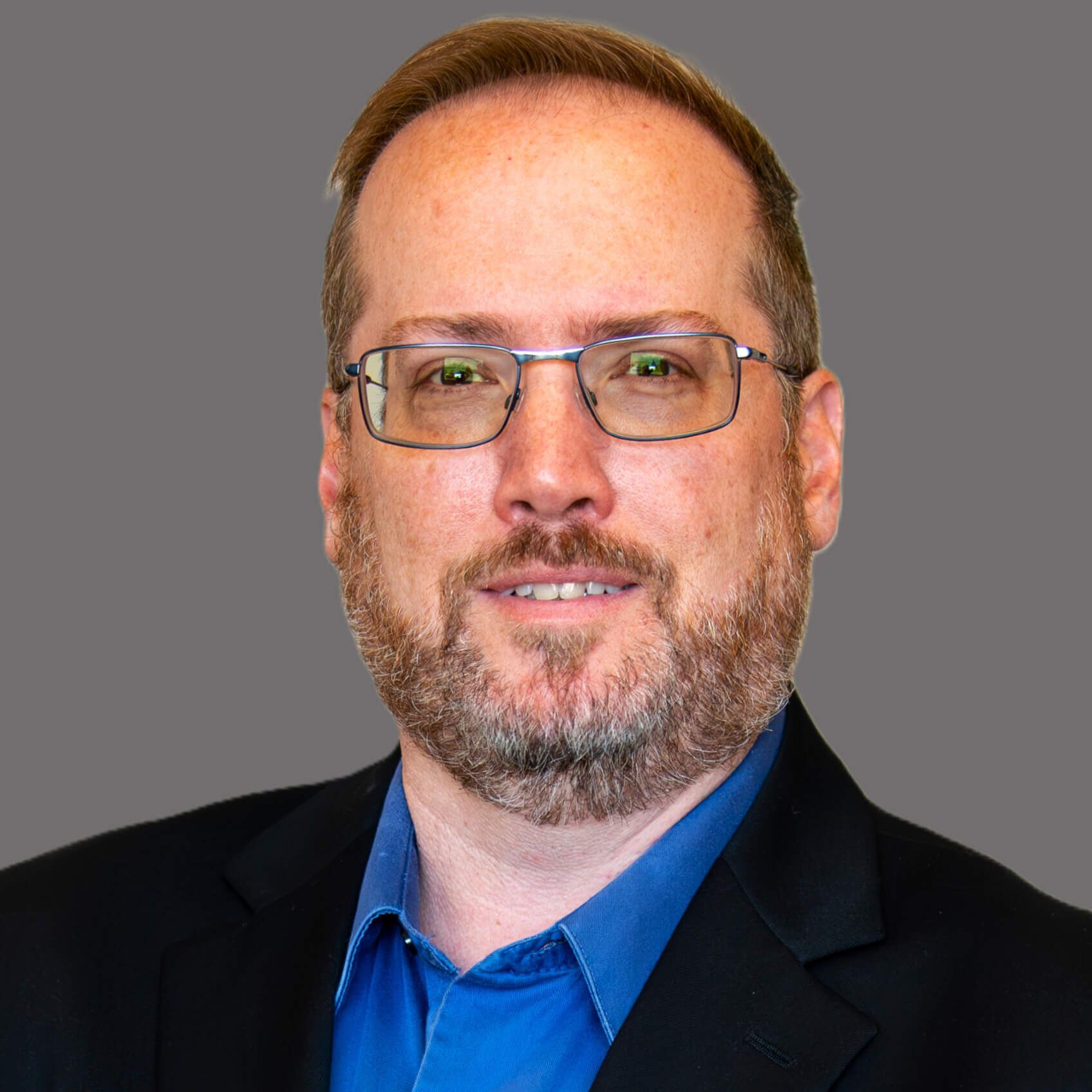 A man with a beard wearing glasses and a blue shirt.