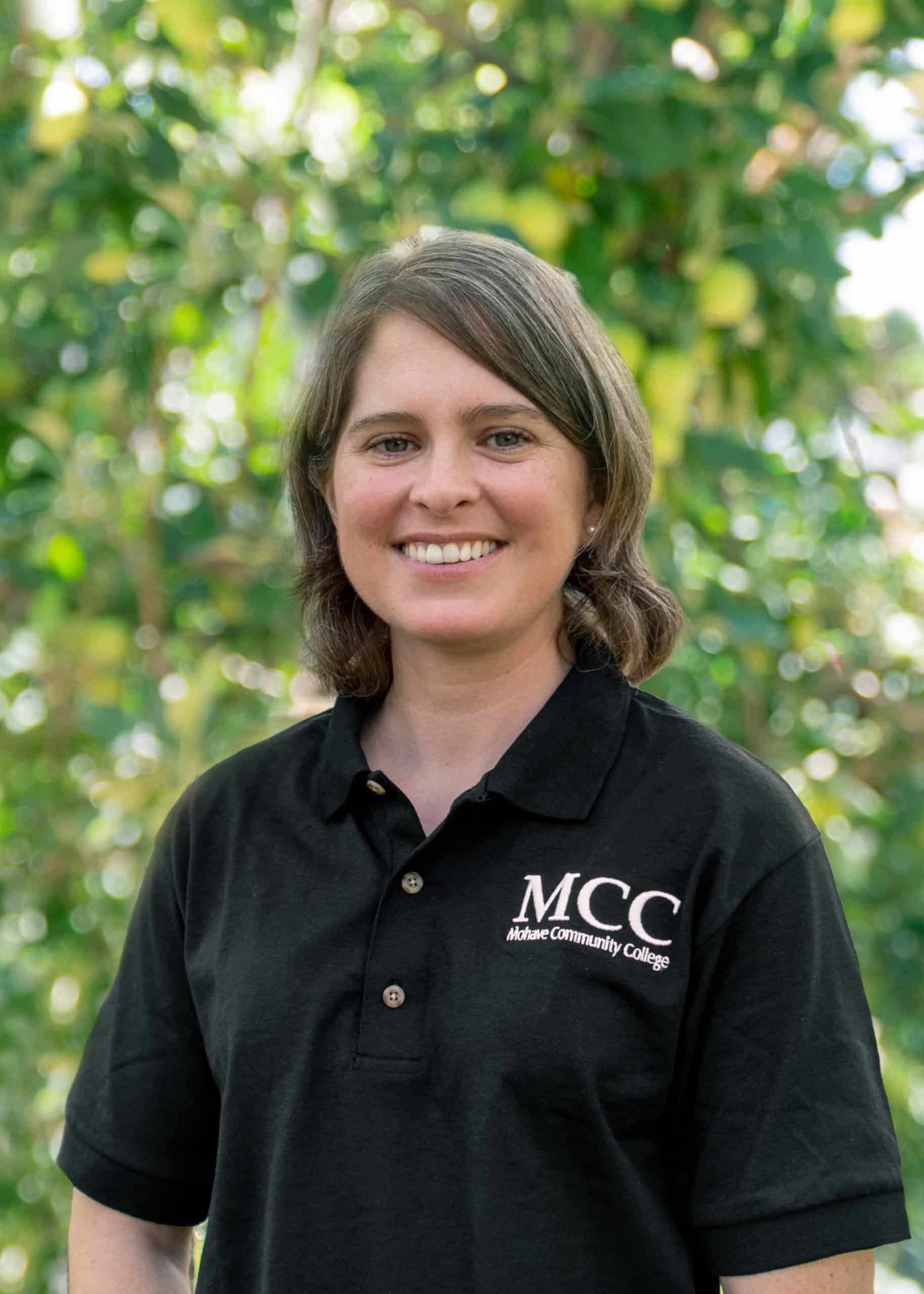A woman wearing a black mcc polo shirt is smiling for the camera.