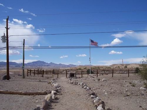 An american flag is flying in the desert near a fence