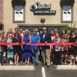 A group of people are standing in front of a building holding a red ribbon.