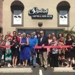A group of people are standing in front of a building holding a red ribbon.