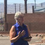 A woman in a blue shirt is standing on the side of the road holding a cell phone.