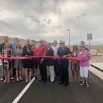 A group of people are standing on the side of a road cutting a red ribbon.