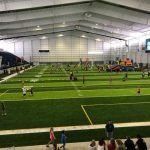 A group of people are standing in front of a large indoor soccer field.