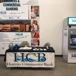 A table with a sign on it is in a room next to an atm.