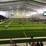 A group of people are standing in a large indoor stadium watching a soccer game.